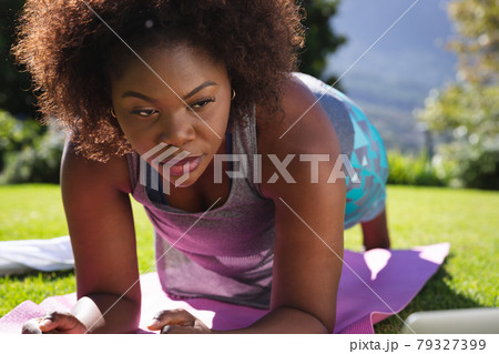 African american woman exercising doing plank on yoga mat in sunny garden African american woman exercising doing plank on yoga mat in sunny garden 79327399