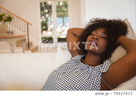 Portrait of african american woman with eyes closed reclining on sofa at home Portrait of african american woman with eyes closed reclining on sofa at home 79327415
