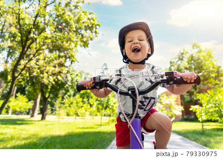 Portrait little cute adorable caucasian toddler boy in safety helmet enjoy having fun riding exercise bike in city park road yard garden forest. Child first bike. Kid outdoors sport summer activities Portrait little cute adorable caucasian toddler boy in safety helmet enjoy having fun riding exercise bike in city park road yard garden forest. Child first bike. Kid outdoors sport summer activities 79330975