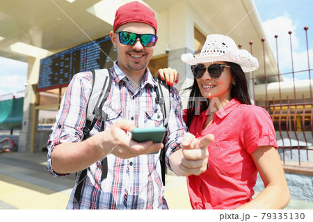 Young man and woman in sunglasses standing on platform of train and looking at screen of mobile phone Young man and woman in sunglasses standing on platform of train and looking at screen of mobile phone 79335130