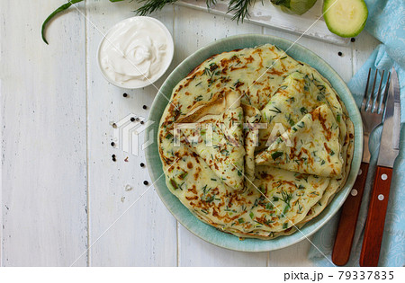 Snack or summer lunch. Zucchini pancakes with greens served with sour cream on a wooden table. Top view flat lay background. Copy space. 79337835