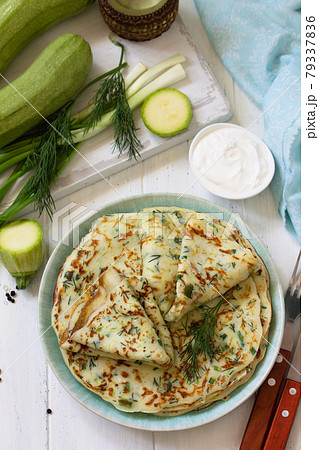 Summer lunch or Snack. Zucchini pancakes with greens served with sour cream on a wooden table. 79337836