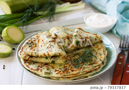 Snack or summer lunch. Zucchini pancakes with greens served with sour cream on a wooden table. 79337837