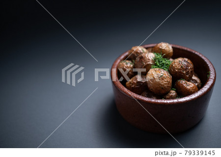 close up of roasted potatoes with herbs in clay bowl on black background 79339145