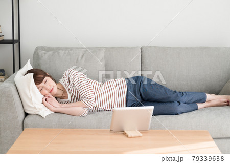 ソファーに寝ながらタブレット端末を見る女性 79339638