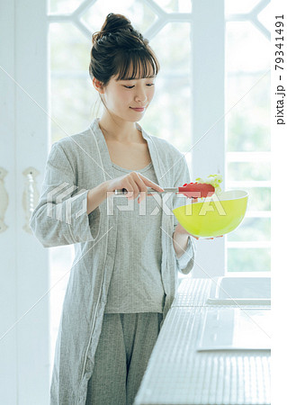 キッチンでサラダを作るトングを持った部屋着の若い女性 79341491