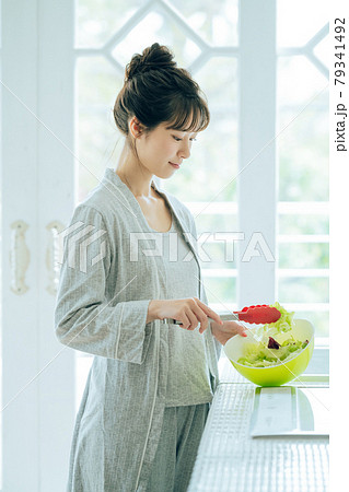 キッチンでサラダを作るトングを持った部屋着の若い女性 キッチンでサラダを作るトングを持った部屋着の若い女性 79341492