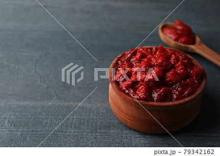 Wooden bowl and spoon with tomato paste on dark wooden background 79342162