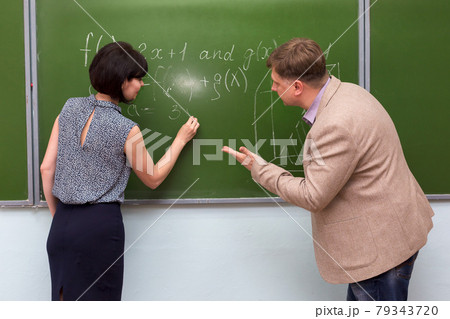 The teacher explains to the student the solution of a math problem at the blackboard The teacher explains to the student the solution of a math problem at the blackboard 79343720