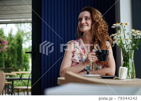 Attractive woman with curly hair drinking coffee sitting at the table in cozy coffee house 79344242