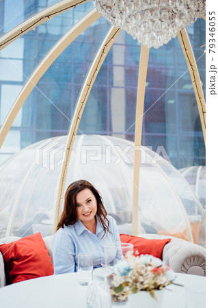 woman in a blue dress sits at tables in a cafe in the shape of a igloo on roof.  79346055