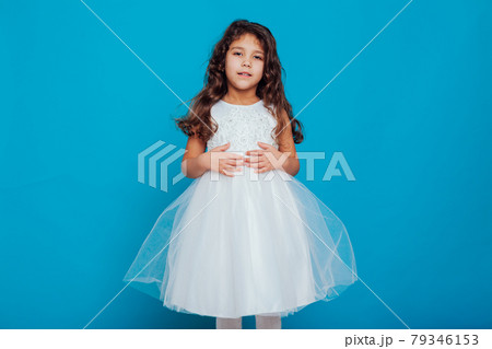 Beautiful little curly girl 5 years old in a white dress on a blue background Beautiful little curly girl 5 years old in a white dress on a blue background 79346153
