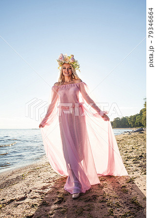 Fashionable woman wearing pink dress and flowers hat on his head on the beach at sunset 79346664