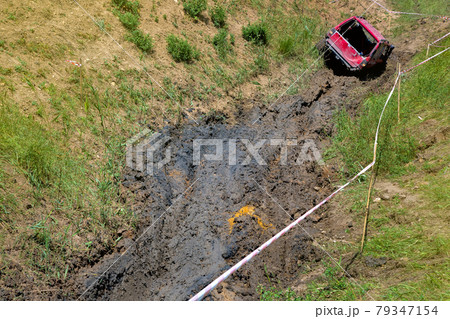 An open pit with slopes and off-road terrain for competition driving through the swamp on off-road vehicles with increased cross-country ability, dirty red car on mud landscape. 79347154