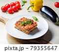 Piece of lasagna on white plate with vegetables 79355647