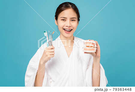 woman wearing braces with tooth and holding toothbrush and dentist tool isolated on blue background. 79363448