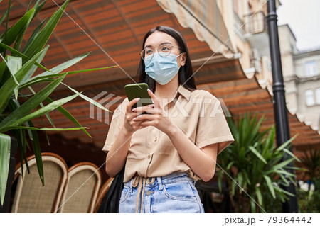 Girl wearing protective mask chatting with somebody at her smartphone 79364442