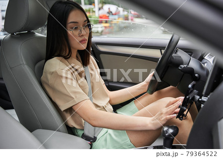 Woman sitting at the car and turning navigator her smartphone before the riding 79364522