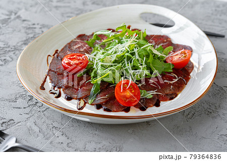 Beef carpaccio with arugula and parmesan on gray surface Beef carpaccio with arugula and parmesan on gray surface 79364836
