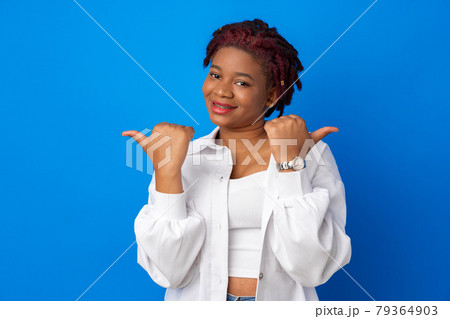 Young african american woman pointing to copy space against blue background 79364903