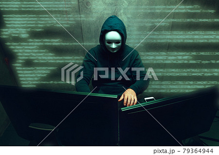 Anonymous hacker wearing face mask working on computer in dark room Anonymous hacker wearing face mask working on computer in dark room 79364944