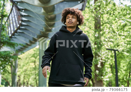 Man wearing earphones while walking at the summer park around the green nature Man wearing earphones while walking at the summer park around the green nature 79366175