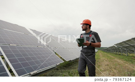 Male engineer with digital tablet PC walking near modern photovoltaic solar panels. Clean energy production. Solar farm. 79367124