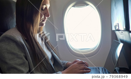 Young woman in a suit typing text on a laptop at the window in an airplane 79368949