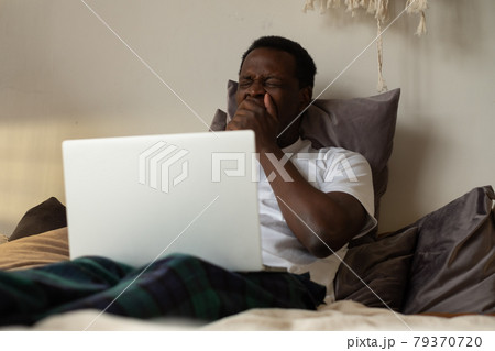 African man working lying on bed at home being tired yawning. 79370720