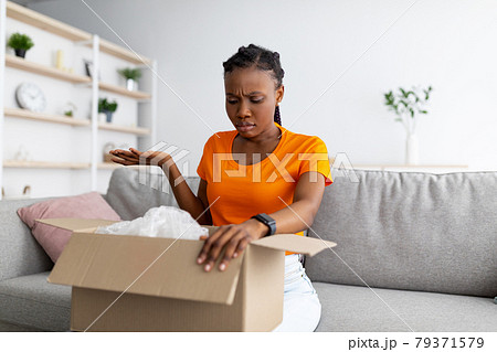 Dissatisfied black woman unpacking cardboard box, receiving damaged item at home. Bad delivery service, online shopping 79371579