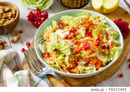 Dietary salad fresh vegetable of Chinese cabbage, carrots, apple, nuts and pomegranate with vinaigrette dressing on a white wooden table. Dietary salad fresh vegetable of Chinese cabbage, carrots, apple, nuts and pomegranate with vinaigrette dressing on a white wooden table. 79372405