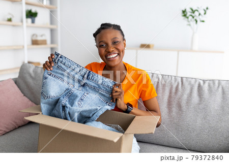 Happy black woman holding jeans, unboxing cardboard package, receiving ordered product, satisfied with her purchase 79372840