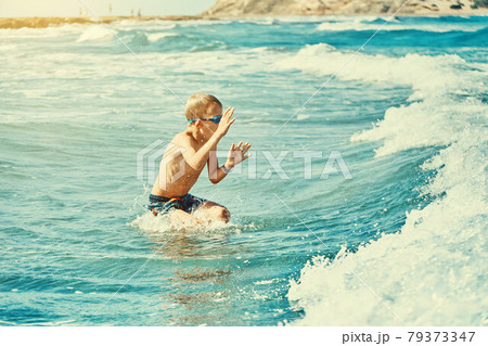 Boy in swimming goggles playing with sea waves 79373347