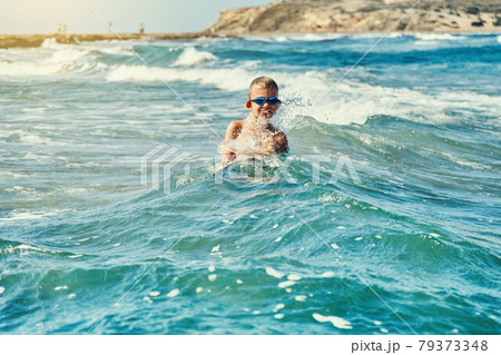 Boy in swimming goggles playing with sea waves 79373348