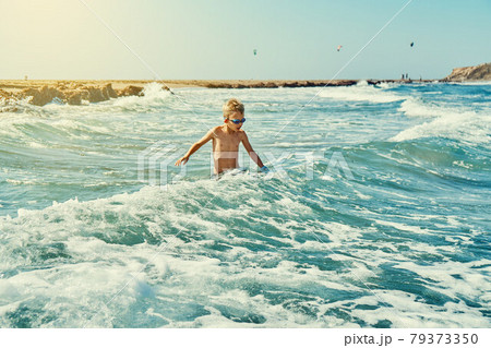 Boy in swimming goggles playing with sea waves 79373350