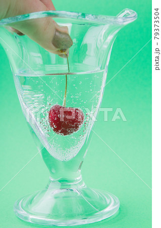 Close-up female hand puts cherry into glass of water. 79373504
