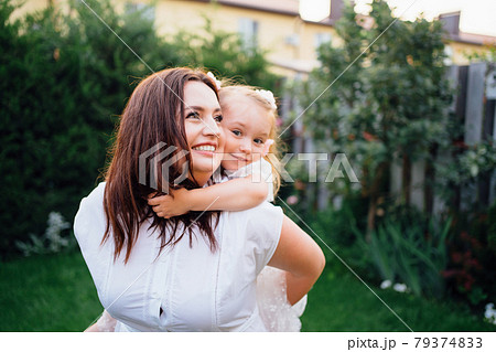 Mom and daughter in white dresses have fun, play and cuddle on the lawn Mom and daughter in white dresses have fun, play and cuddle on the lawn 79374833