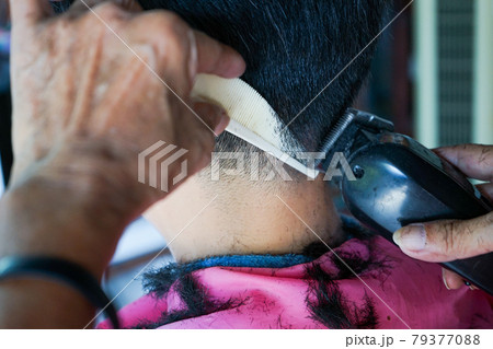 Closeup hands of hairsltylist and rear view of man having a hair cut by electrical battalion. 79377088
