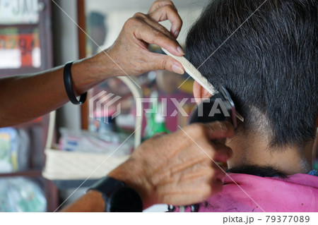 Closeup hands of hairsltylist and rear view of man having a hair cut by electrical battalion. 79377089