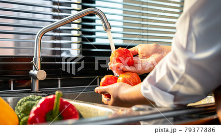 Hands of asian housewife washing tomato and vegetables with water in sink while wearing apron Hands of asian housewife washing tomato and vegetables with water in sink while wearing apron 79377886