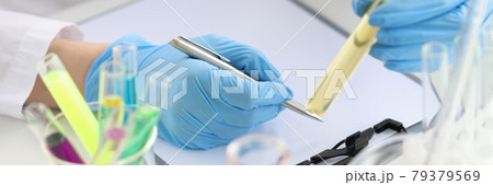 Scientist chemist holding test tube with yellow liquid in his hands and writing in documents closeup Scientist chemist holding test tube with yellow liquid in his hands and writing in documents closeup 79379569