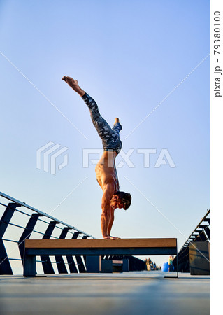Fit man doing a hand stand while practicing yoga alone near the ocean against sky at dusk or dawn 79380100