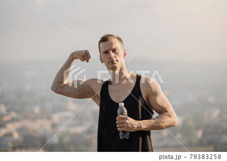 Male athlete demonstrating his muscular biceps to camera, posing outdoors Male athlete demonstrating his muscular biceps to camera, posing outdoors 79383258