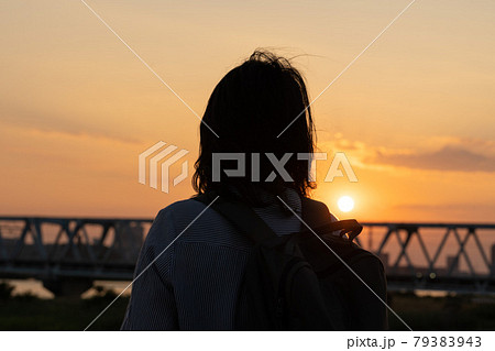 夕日を背景にした女性の後ろ姿のシルエットの写真素材