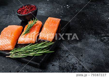 Raw salmon fillet steaks on marble board with herbs. Black background. Top view. Copy space Raw salmon fillet steaks on marble board with herbs. Black background. Top view. Copy space 79387227