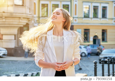 Urban portrait of beautiful young blonde woman with long hair flying in wind 79390158