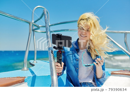 Young woman recording stream on smartphone sitting on board of yacht in sea Young woman recording stream on smartphone sitting on board of yacht in sea 79390634