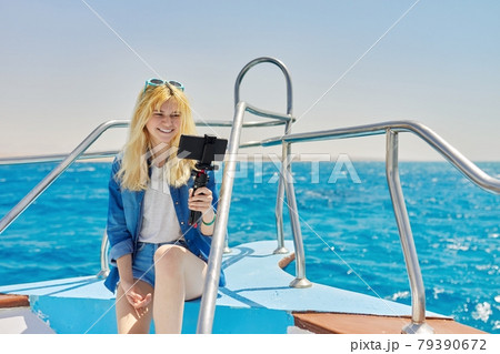 Young woman recording stream on smartphone sitting on board of yacht in sea Young woman recording stream on smartphone sitting on board of yacht in sea 79390672