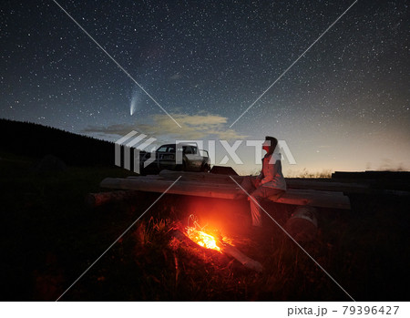 Female traveler sitting near campfire under night starry sky. 79396427