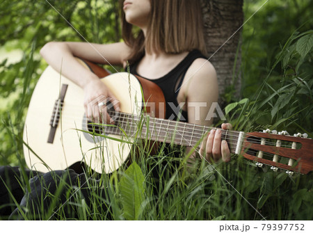 Teenager girl playing guitar in park 79397752